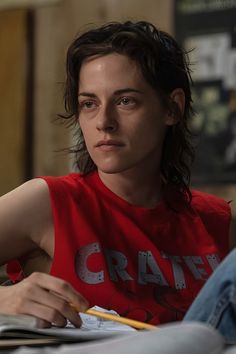 a woman in a red shirt sitting at a table with a notebook and pencils