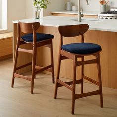 two wooden barstools with blue cushions sit in front of a kitchen countertop