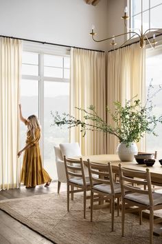 a woman standing in front of a window next to a dining room table and chairs