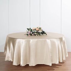 a round table with a flower centerpiece on it's top, in front of a white wall