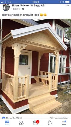 a small wooden house with porch and stairs on the front steps, next to a red building