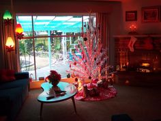 a living room filled with furniture and a christmas tree next to a fire place in front of a window