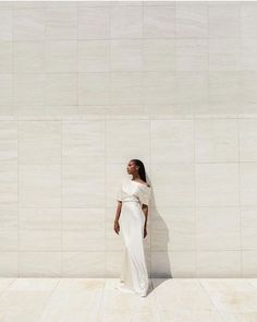 a woman standing in front of a wall with her back to the camera, wearing a white dress