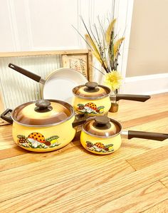 three yellow pots and two pans are on the floor next to a vase with flowers