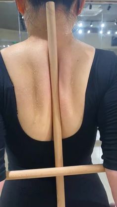 the back of a woman holding a wooden stick in her right hand and wearing a black top