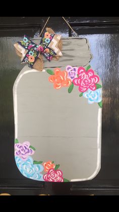 a painted mason jar with flowers on it hanging from a door hanger in front of a mirror