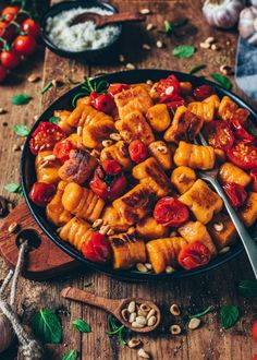 a bowl filled with pasta and tomatoes on top of a wooden table next to other food