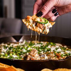 a person taking a slice of pizza from a skillet with tortilla chips