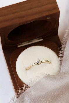 an engagement ring in a wooden box with a white cloth on the floor next to it