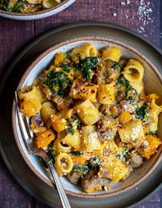 two bowls filled with pasta and spinach on top of a wooden table next to silverware