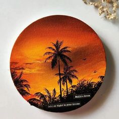 an orange sunset with palm trees painted on the front and back of a round coaster