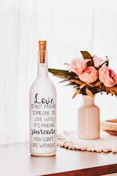 a bottle that is sitting on a table with some flowers in the vase behind it