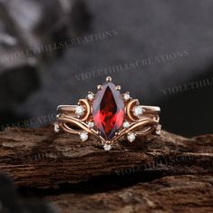 a ring with a red stone and white diamonds on it sitting on top of a rock