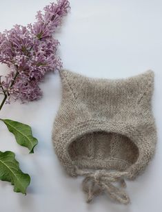 a knitted hat next to purple flowers on a white surface