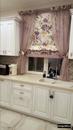 a kitchen with white cabinets and floral curtains