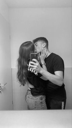 a man and woman standing in front of a bathroom mirror taking a selfie with their cell phone