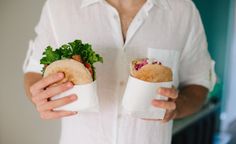 a man holding two burritos in his hands while standing next to each other