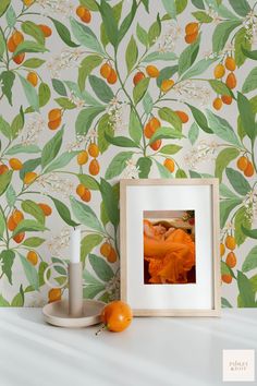 an orange sitting on top of a white shelf next to a wallpaper covered in leaves