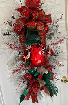 a red and green christmas wreath hanging on the front door with bells, ornaments and ribbons