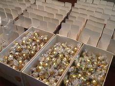 boxes filled with gold and silver ornaments on top of a wooden table in front of rows of white chairs