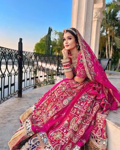 a woman in a pink bridal gown sitting on a ledge with her hand under her chin