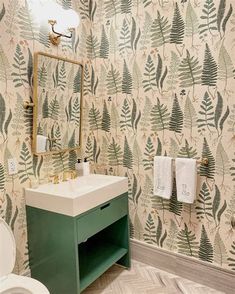 a bathroom with a sink, toilet and wallpaper in green tones on the walls