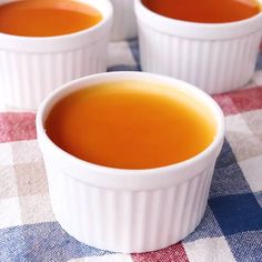 three small white bowls filled with soup on top of a checkered table cloth next to two spoons