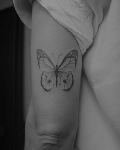 a black and white photo of a butterfly tattoo on the right arm, which is sitting on someone's leg