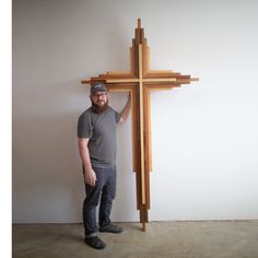 a man standing next to a wooden cross on the floor in front of a wall