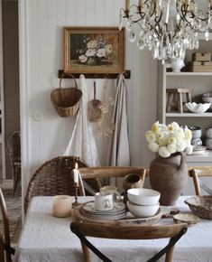 a dining room table with plates, cups and saucers on it in front of a chandelier