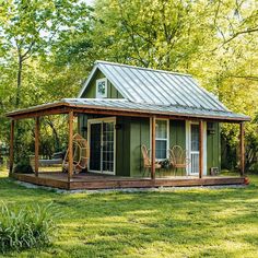 a small green house with a metal roof in the middle of a grassy area surrounded by trees