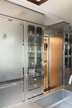 a kitchen with stainless steel cabinets and glass shelves on the wall, along with a sink