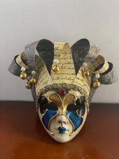 This Maschera del Galeone mask is a beautiful piece of art that can be displayed on a wall or a shelf in your home and, over time, will become a special conversation piece for you and your guests.  Please NOTE all Venetian masquerade masks are handcrafted and fashioned after original designs developed in Italy during the 16th and 17th centuries with the "Comedia del 'Arte".  These Venetian mask art pieces are authentically handmade/hand decorated and imported from the finest design studios in Venice, Italy. It is pre-owned but shows very little wear.  The braiding is not frayed or torn, the pearls and gold balls are intact, and the colors are lovely and have no scratches or stains.  Also, there are NO chips or stains on the face of the mask. It is in excellent condition. The measurements f Handmade Artistic Masks For Carnival, Artistic Masks For Carnival Gift, Artistic Carnival Masks As Gifts, Artistic Masquerade Mask For Festivals, Artistic Masks And Prosthetics For Mardi Gras, Artistic Handmade Masks For Mardi Gras, Artistic White Masks As Gifts, Artistic White Masks As A Gift, Handmade Masks For Carnival Gift