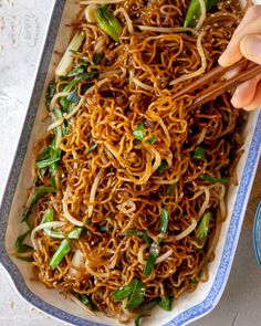 someone holding chopsticks over a plate of noodles