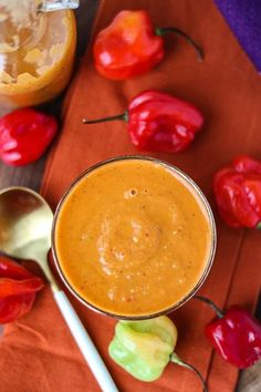 a close up of a bowl of hot sauce with spoons and peppers in the background