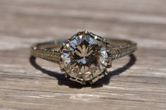 an old - fashioned engagement ring with a fancy diamond center sits on a wooden surface