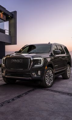 the front end of a black gmc suv parked in front of a building at sunset