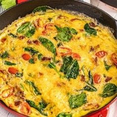 an omelet with spinach and tomatoes in a red pan on a table