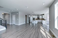 an empty kitchen and living room in a house with hardwood floors, white cabinets, and stainless steel railings