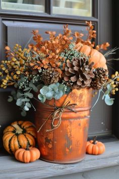 an orange pail filled with lots of flowers and pine cones on top of a window sill