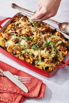 a red casserole dish filled with vegetables and cheese being spooned into it