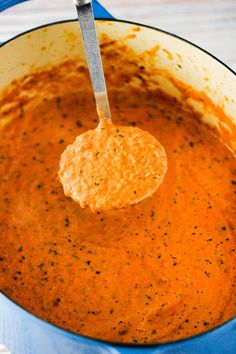 a ladle full of tomato soup with a spoon in it