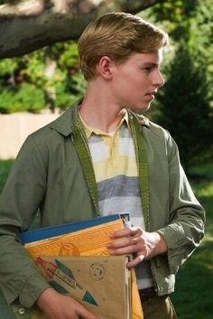 a young man holding papers and folders in his hands while standing next to a tree