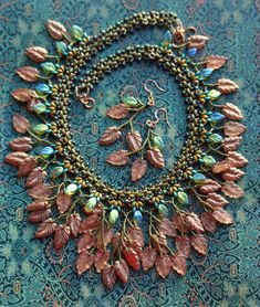 a close up of a necklace and earring on a blue cloth with gold leaves