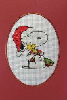 a cross stitch picture with a snoopy christmas hat and scarf