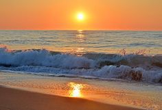 the sun is setting over the ocean with waves crashing on the shore and in the foreground