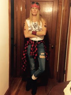 a woman with her arms crossed standing in front of a door wearing ripped jeans and a bandana