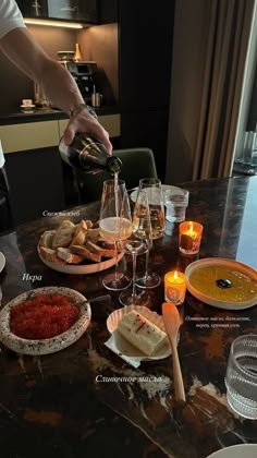 a person pouring wine into some glasses on a table with food and candles in front of them