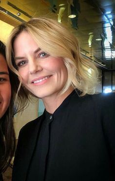 two women posing for the camera with one woman smiling at the camera, both wearing black