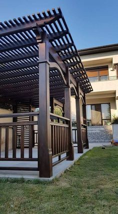 a wooden pergola sitting on top of a lush green field next to a building